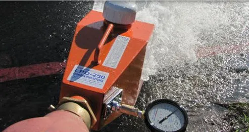 Close-up of an orange device attached to a hose, releasing water under pressure with a pressure gauge visible.