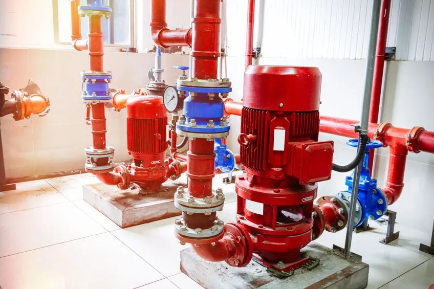 Red industrial water pumps connected to red and blue piping inside a clean mechanical room with tiled floor.