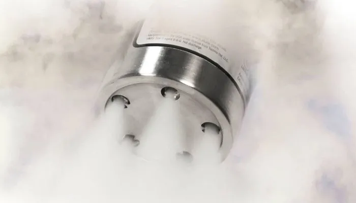 Close-up of a stainless steel container emitting thick white vapor or fog from multiple small holes.