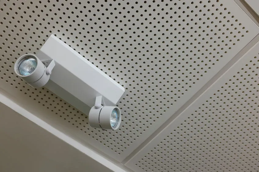 White dual spotlight fixture mounted on a perforated ceiling.