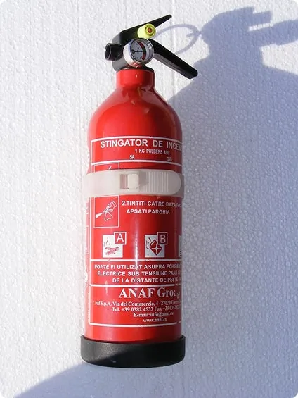 Red fire extinguisher mounted on a white wall casting a shadow.