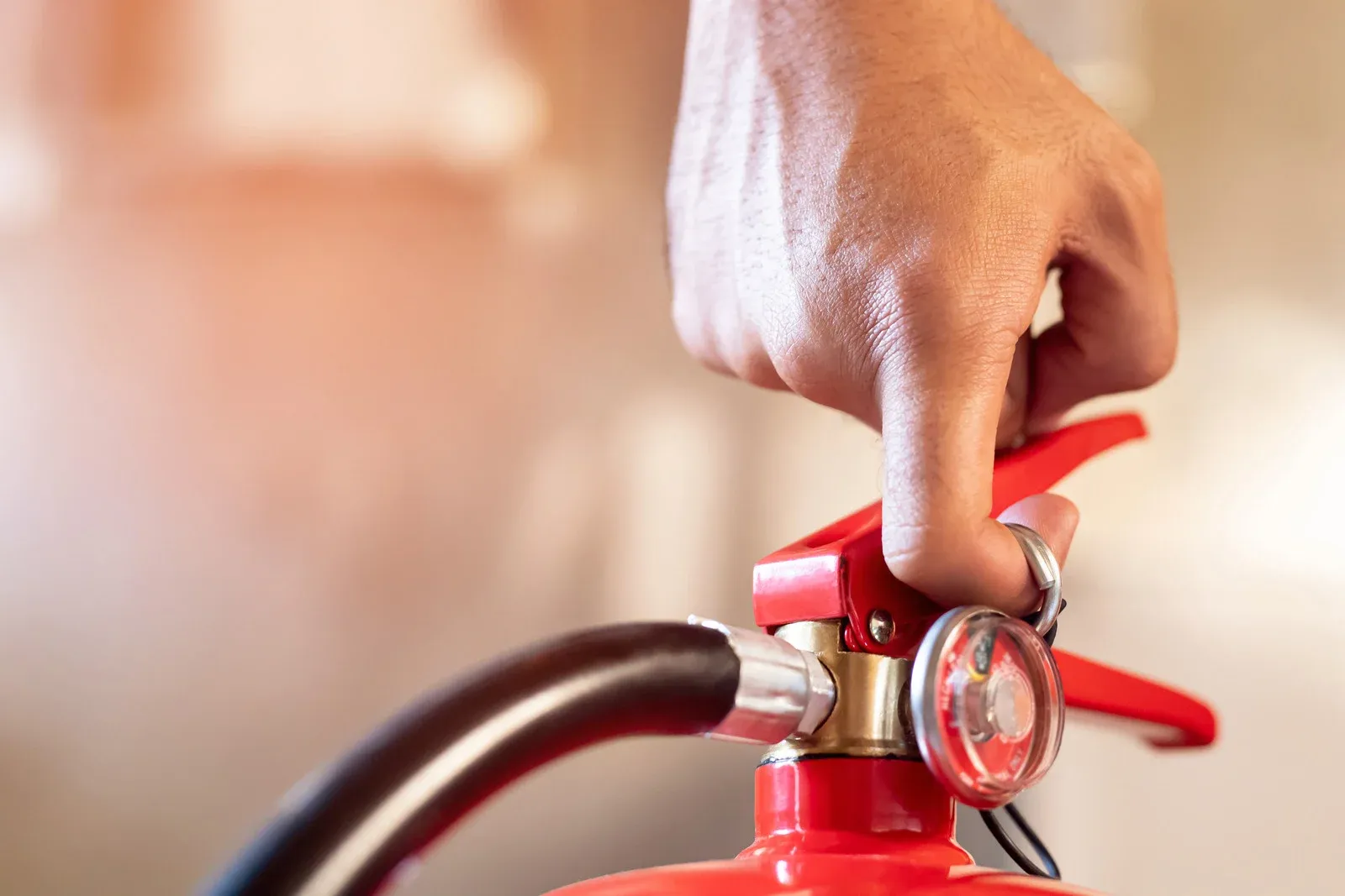 Close-up of a hand gripping the handle and safety pin of a red fire extinguisher.