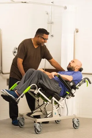 Carer assisting a man in a tilting shower chair