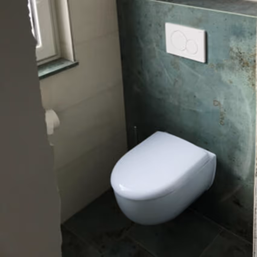 Helles WC mit Betonoptikwand, wandhängender Toilette und kleinem Fenster.