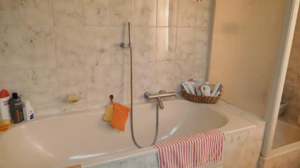 Älteres Bad mit weißer Wanne, beige-grauen Fliesen und bunter Dekoration.