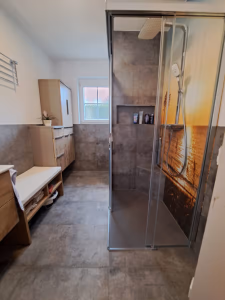 Modernes renoviertes Bad mit Holzoptikfliesen, Glasdusche und hellen Wänden.