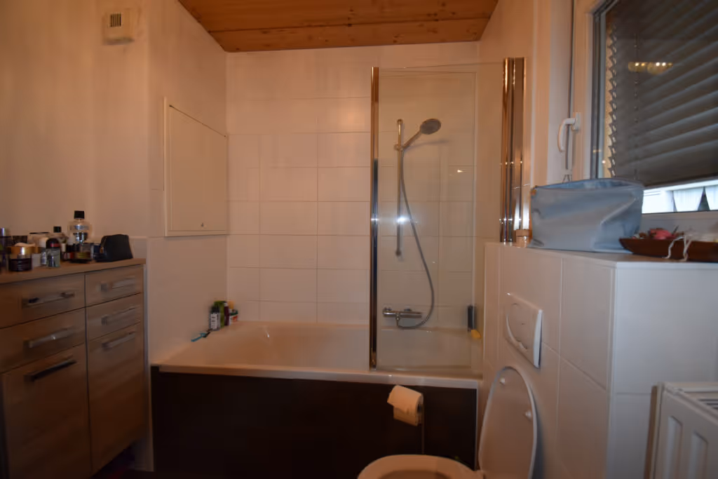 lteres Bad mit Holzdecke, brauner Badewanne und Dusche vor der Sanierung.