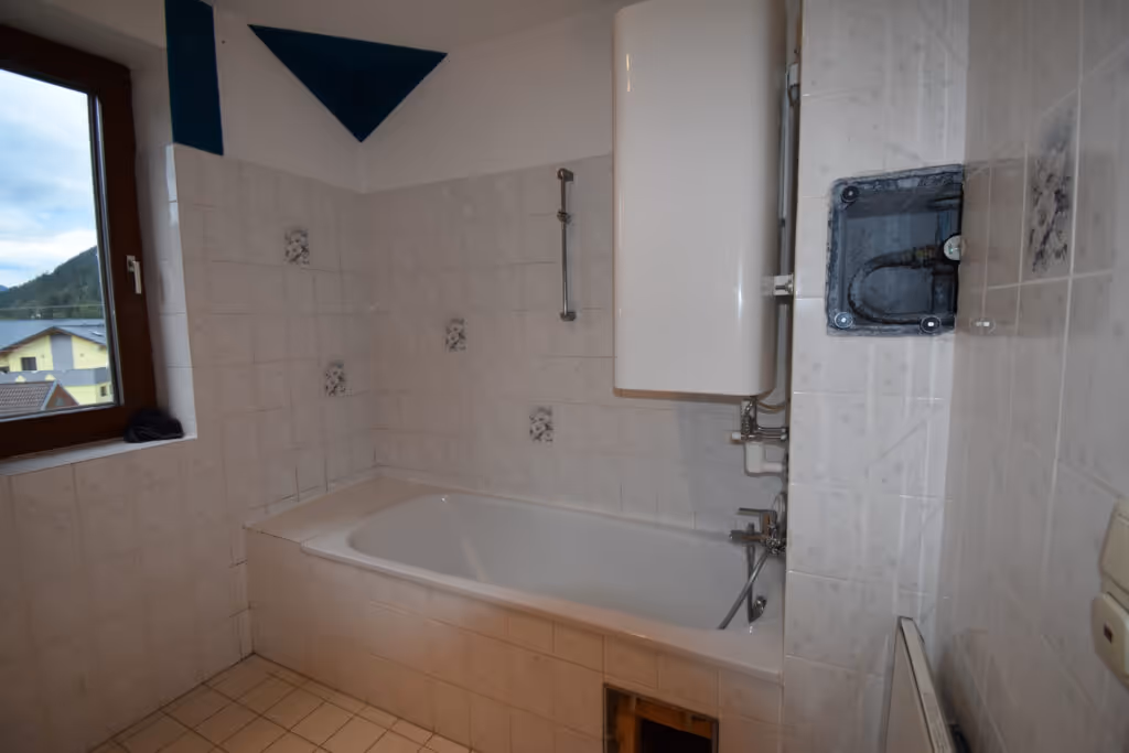 Altes, weiß gefliestes Bad mit Badewanne und kleinem Fenster.