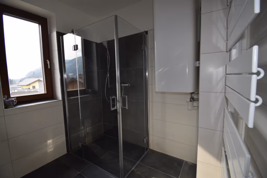 Großes, renoviertes Bad mit Glasdusche und Fenster, dunklem Boden und hellen Wänden.