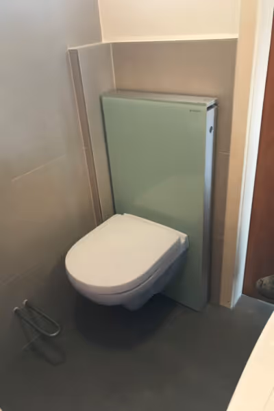 Modernes WC mit Milchglaswand und grauen Bodenfliesen.