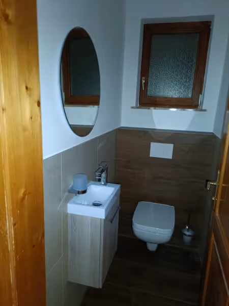 Altes Bad mit Holztür, kleinem Waschbecken und braunen Wandfliesen.