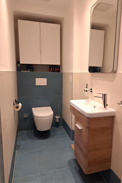 Modernes, helles Bad mit weißen Möbeln, Holzunterschrank und grauen Bodenfliesen.