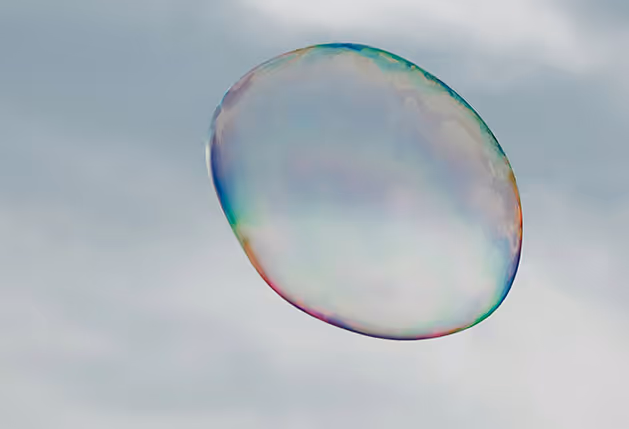 Eine Seifenblase fliegt durch die Luft, im Hintergrund sind Wolken.
