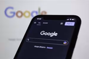 Ein Smartphone mit der Google Suche geöffnet, im Hintergrund unscharf das Google-Logo.