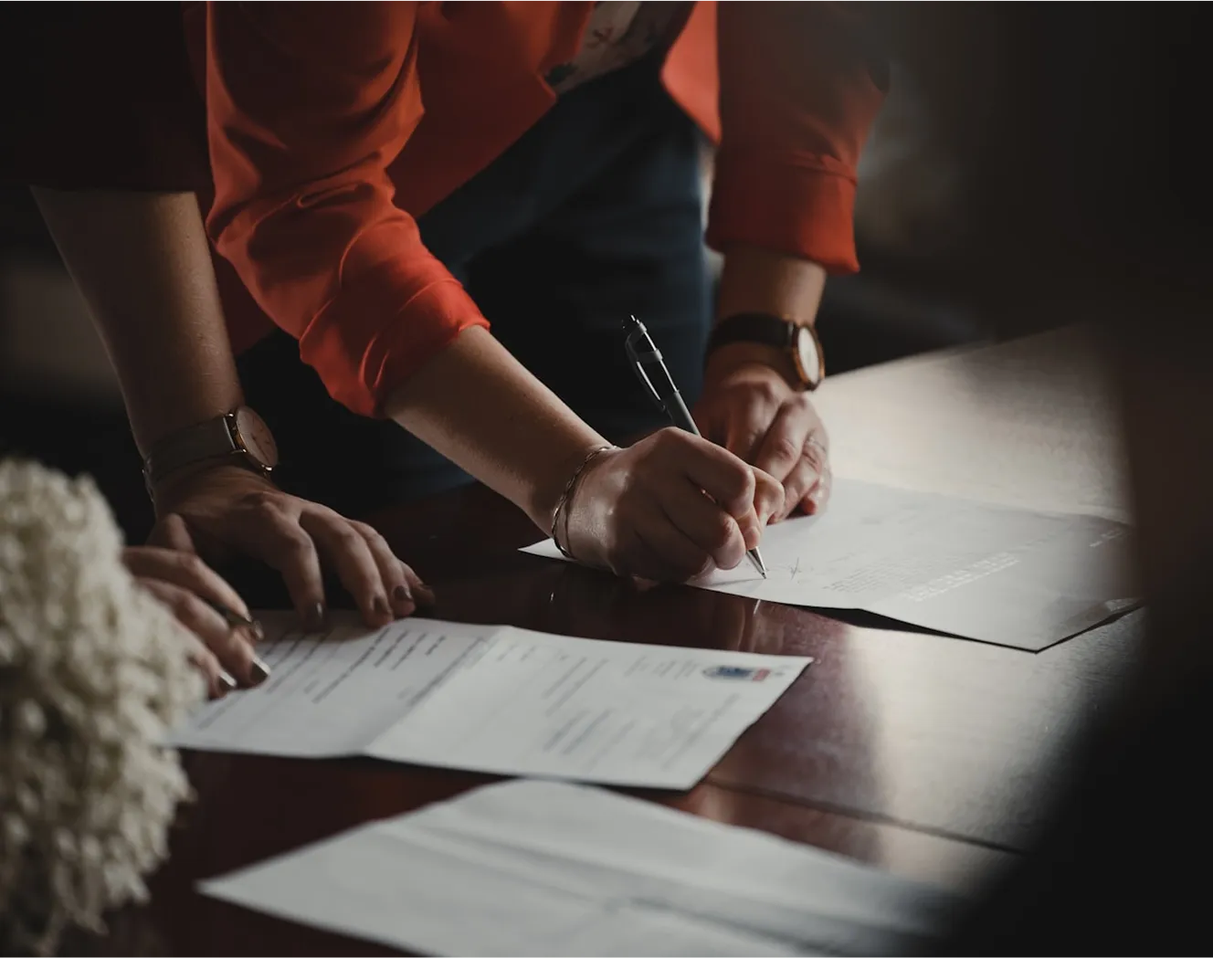 Person in red shirt signing document at desk with multiple papers