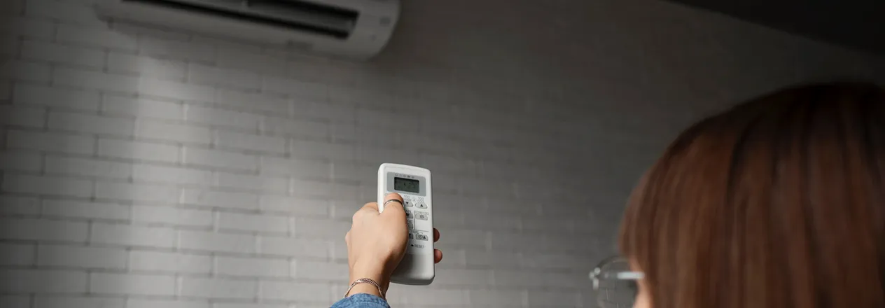 Hand holding air conditioner remote control against white brick wall