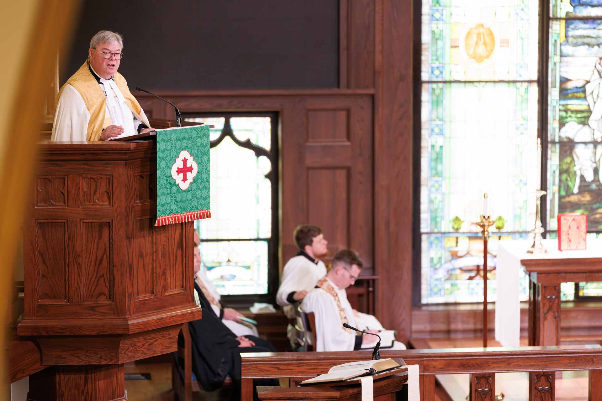 Priest preaching from the pulpit in Trinity’s chapel with stained glass, highlighting worship and preaching resources.
