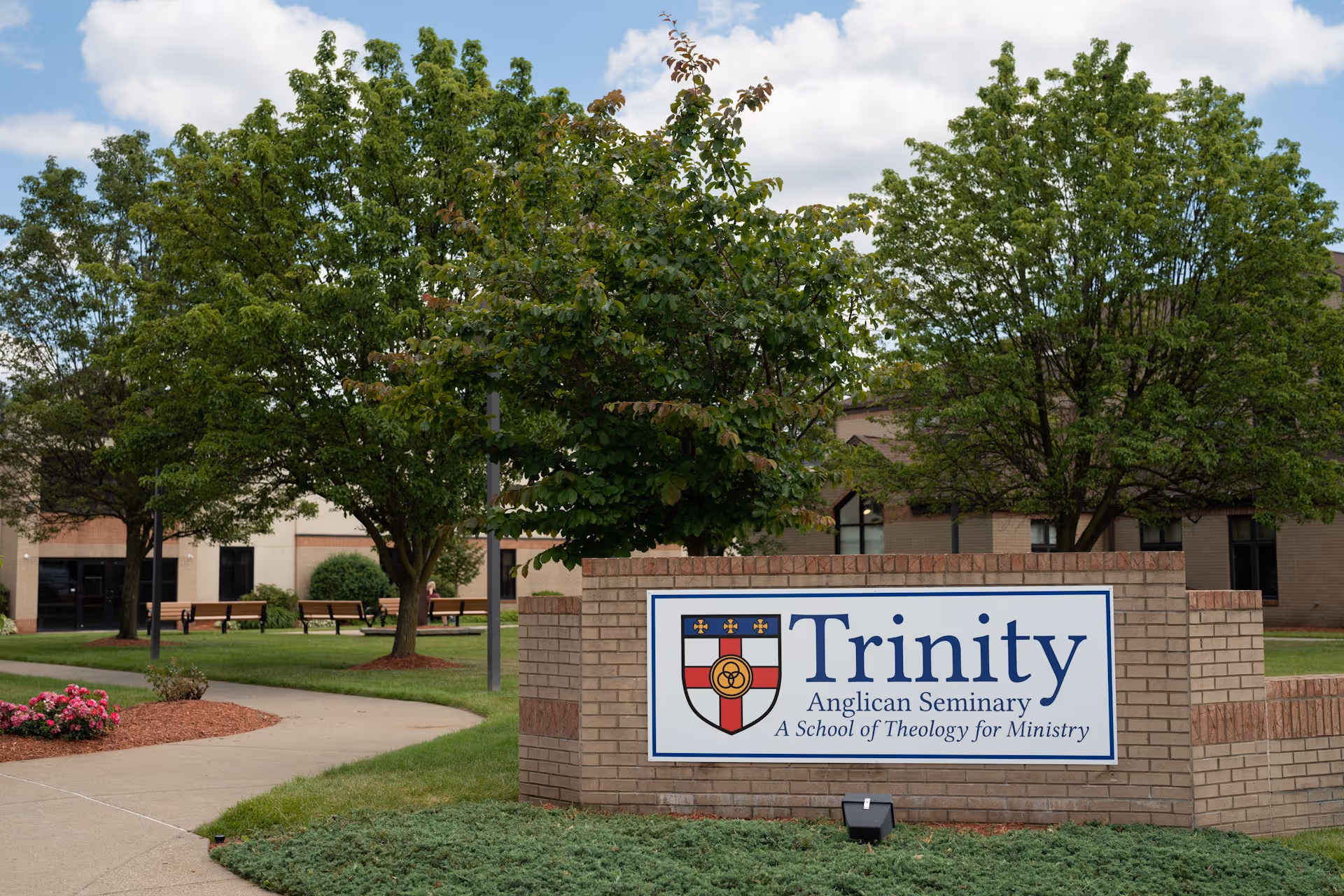 Brick campus sign reading “Trinity Anglican Seminary” outside academic buildings.