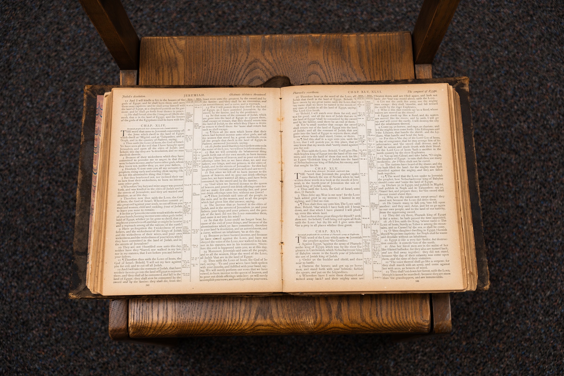 Open old book with text pages on a wooden chair over dark carpet.