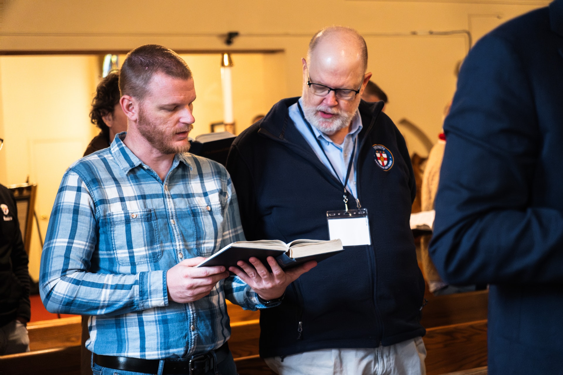 Two men standing and reading a book together inside a church.
