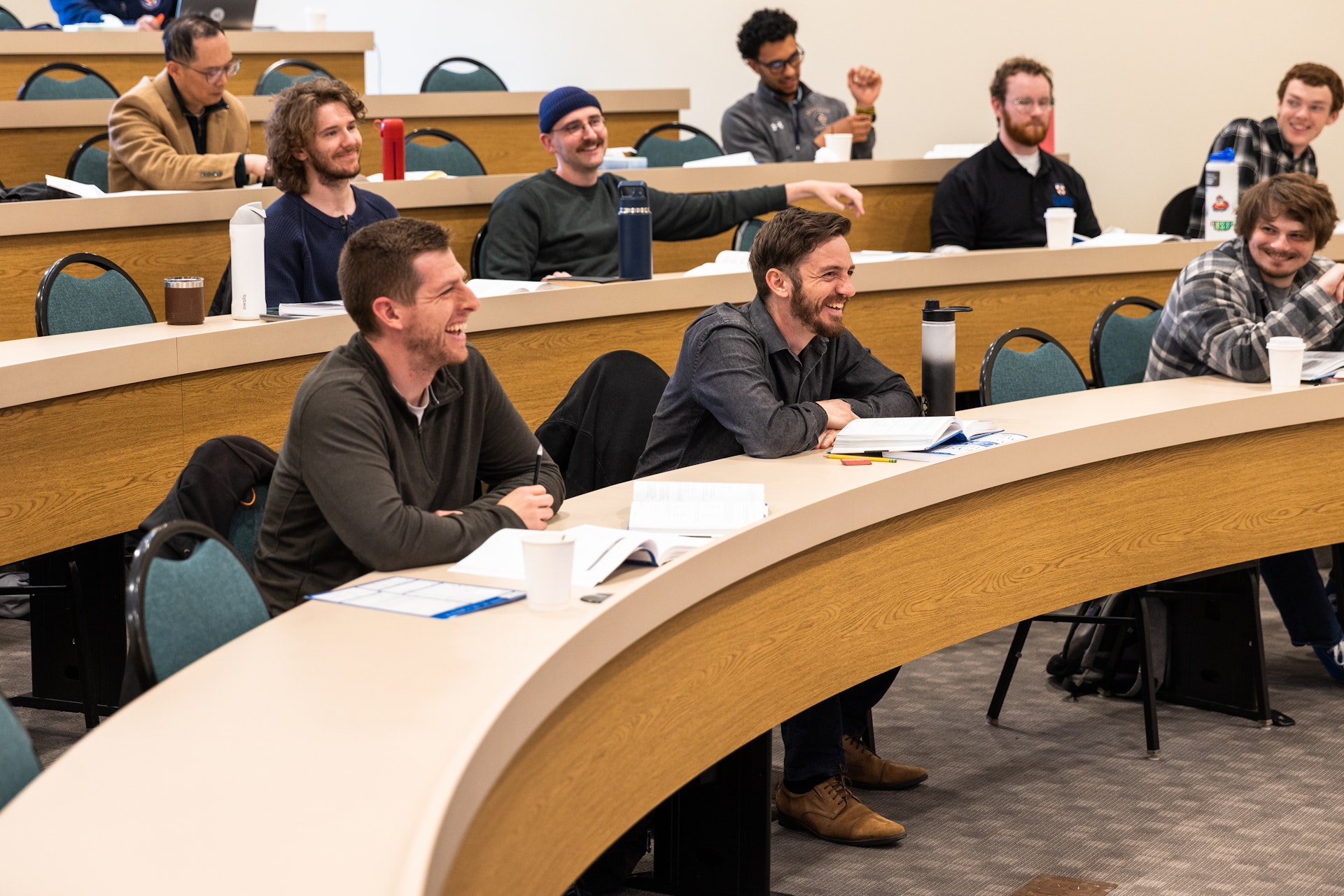 Group of male students in a lecture hall smiling and engaging during class.