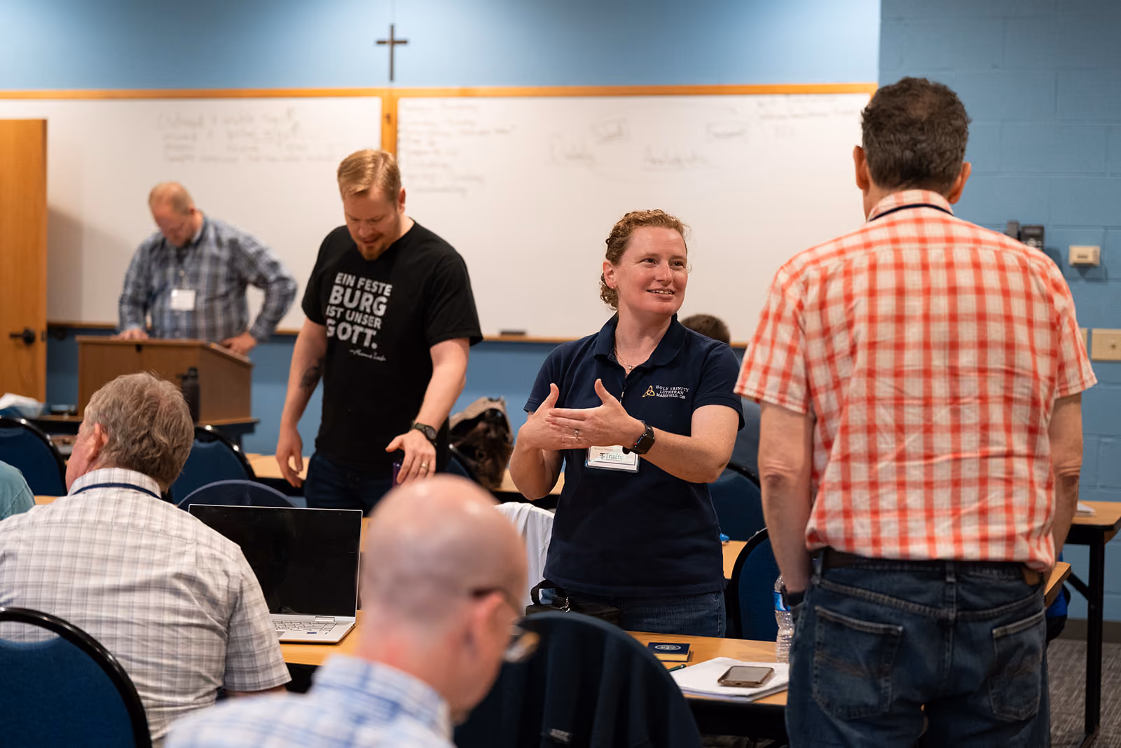 Group of people engaging in discussion during a workshop in a classroom. A woman speaks animatedly to a man. The atmosphere is focused and collaborative.