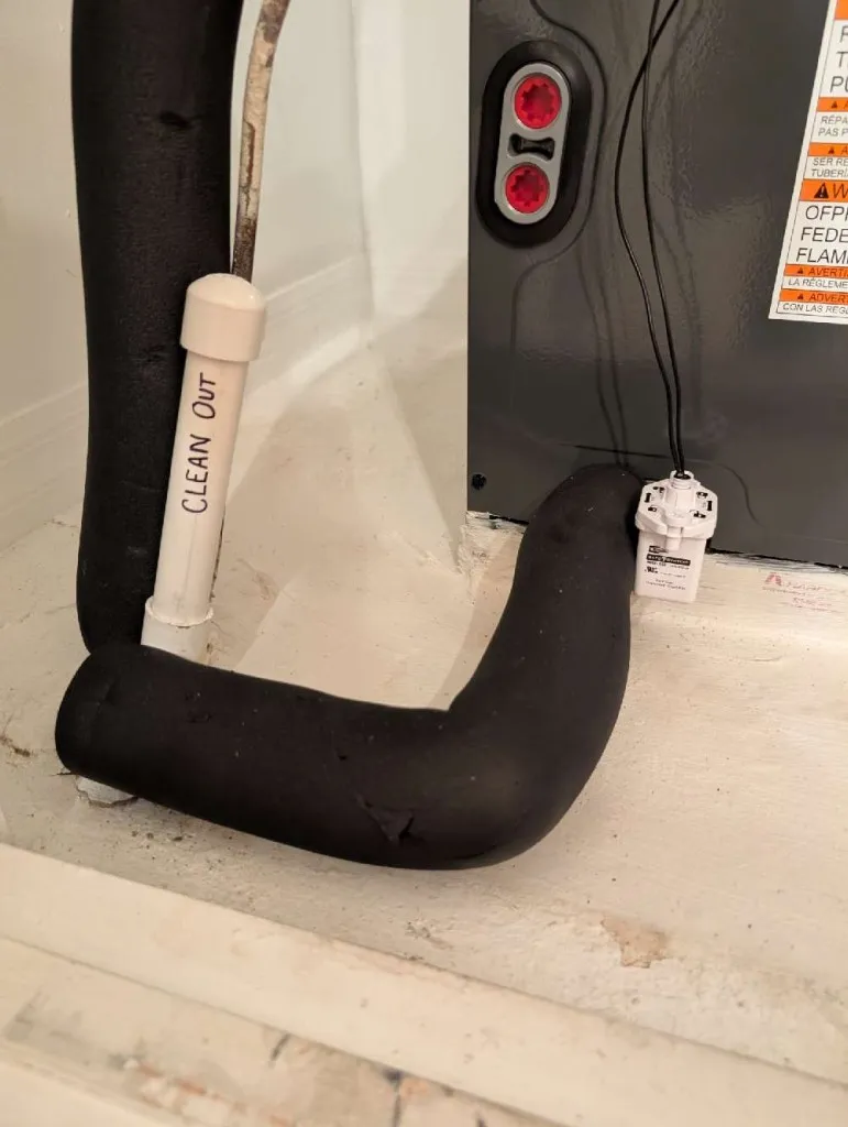 Black curved pipe with "Clean Out" label near electrical equipment