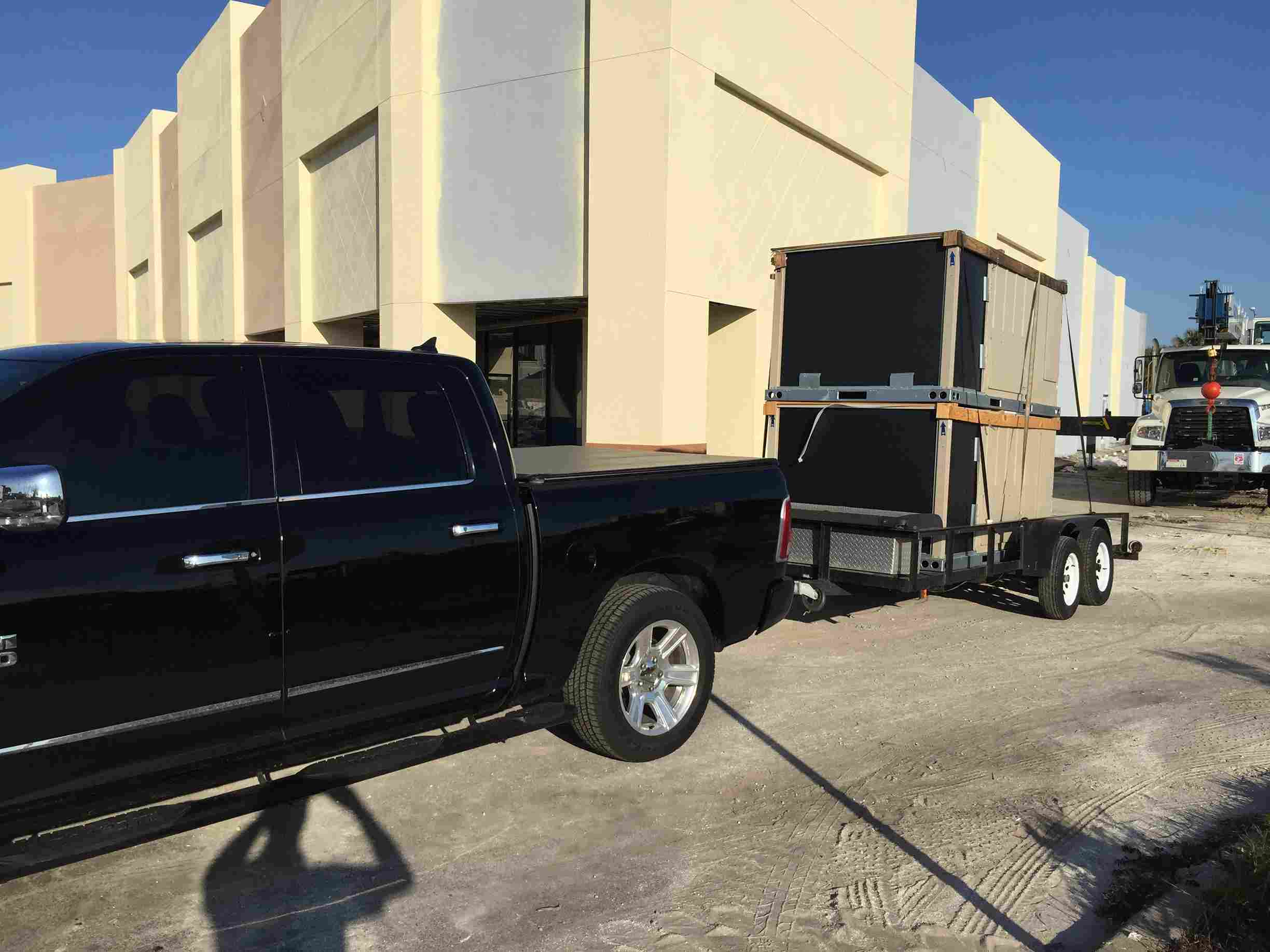 Black pickup truck towing a trailer near modern white building