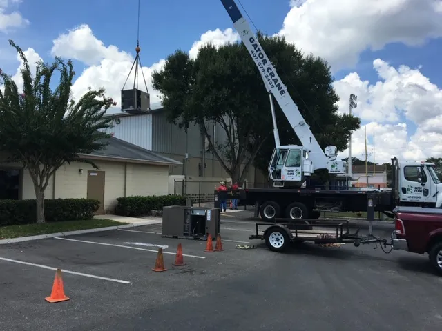 Mobile crane lifting equipment in parking lot near building on cloudy day