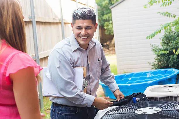 Smiling technician servicing air conditioning unit outdoors near blue pool