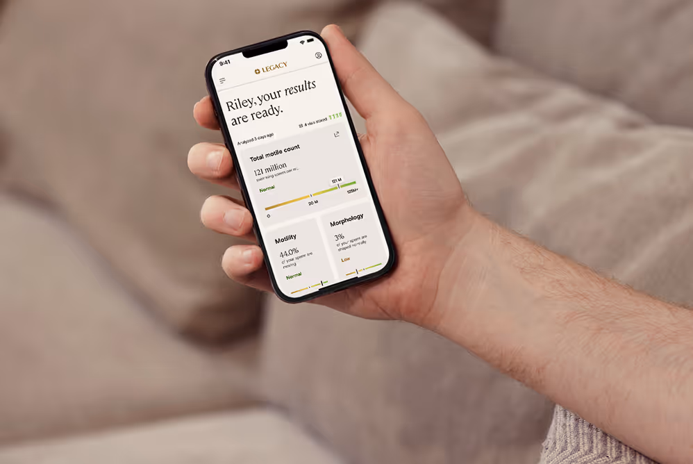 A person holding a smartphone displaying Legacy app with sperm analysis results showing total motile count, motility, and morphology.