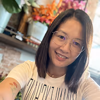 Smiling woman with glasses and shoulder-length hair taking a selfie indoors with blurred background of flowers and decor.