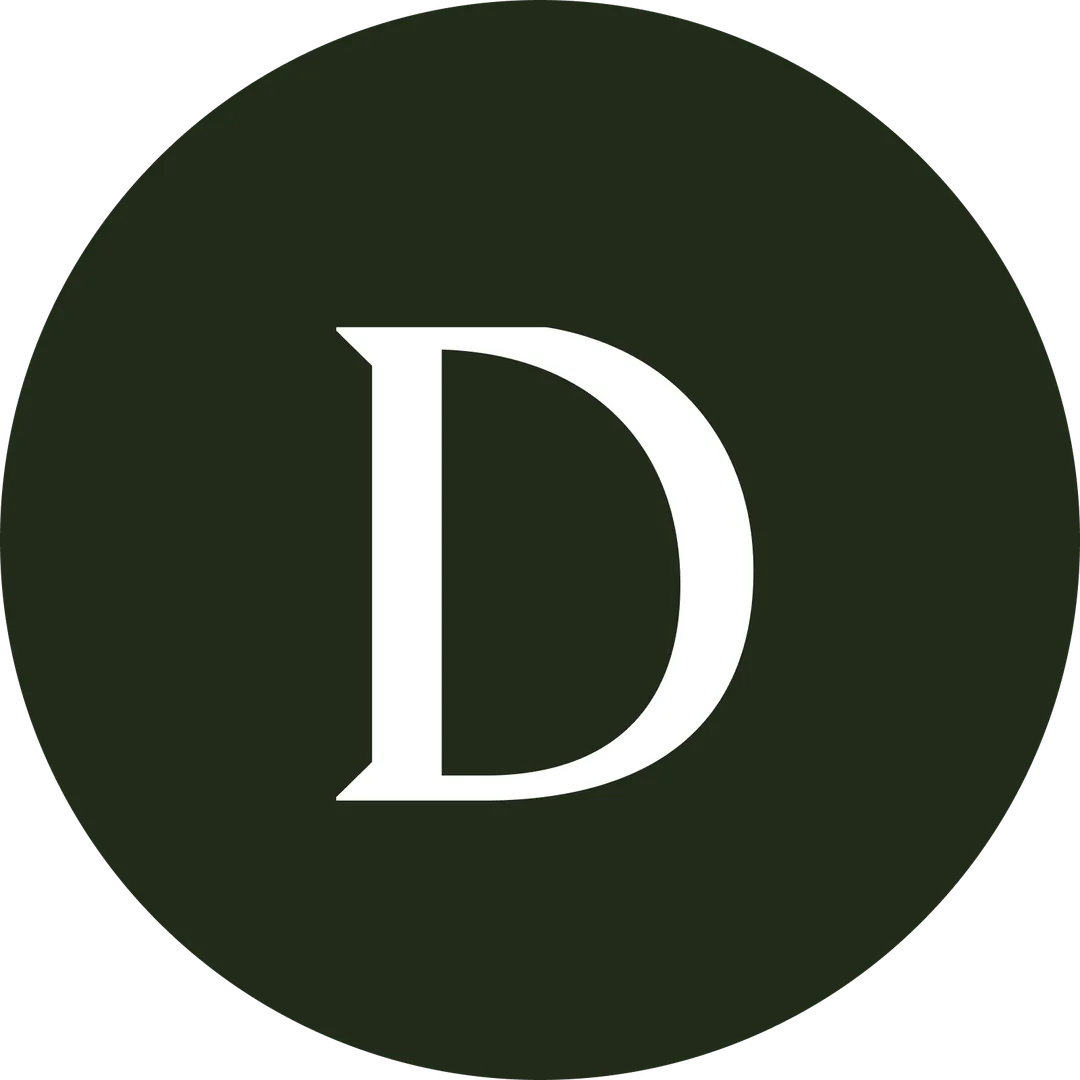 A smiling man and woman pose closely together for a selfie. The man has short curly hair, a beard, and a nose ring, while the woman has long curly hair and is wearing hoop earrings. They are sitting in front of a tiled wall with potted plants in the background. The image is black and white and cropped into a circular frame.