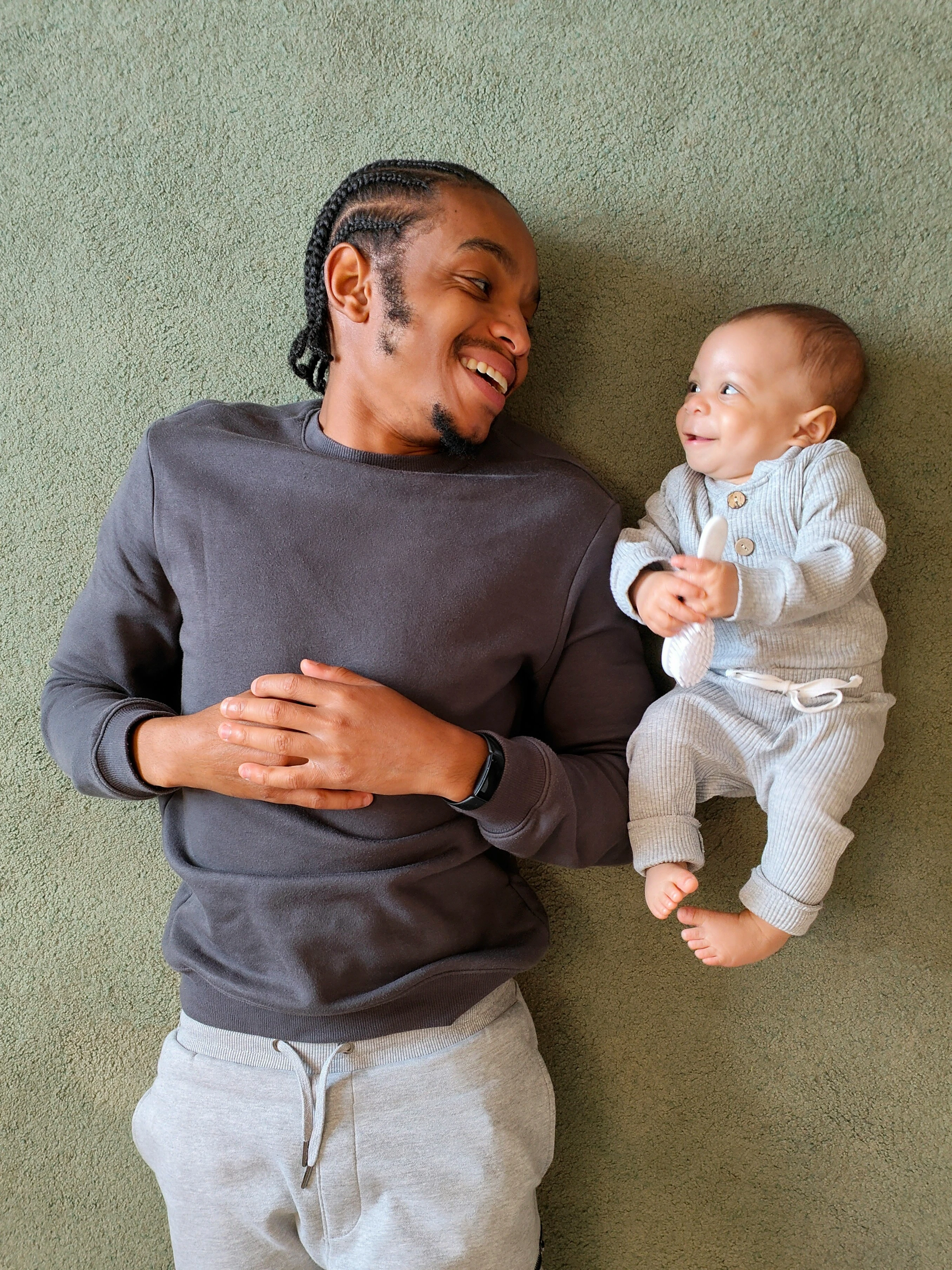 Smiling father in purple sweater lying on floor with baby in white outfit, playful bonding moment indoors