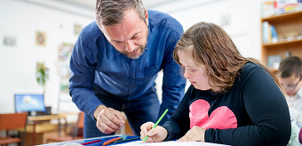 A teacher leaning over a neurodivergent teen girl's desk
