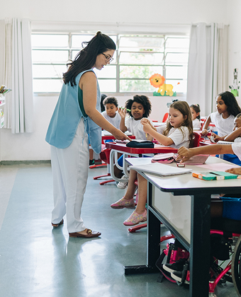 A female teacher standing at the front of a classroom full of children