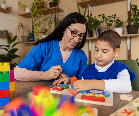 A female teacher working with a young boy to put together a puzzle