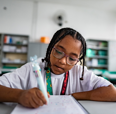 A young girl with braids sitting in her classroom writing in a notebook