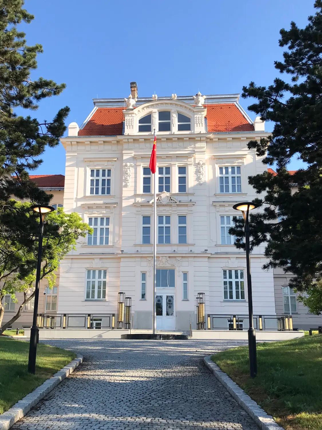 Priečelie budovy s červenou strechou, symetricky osadené bielymi rustikálnymi oknami okolo stredového vstupu.