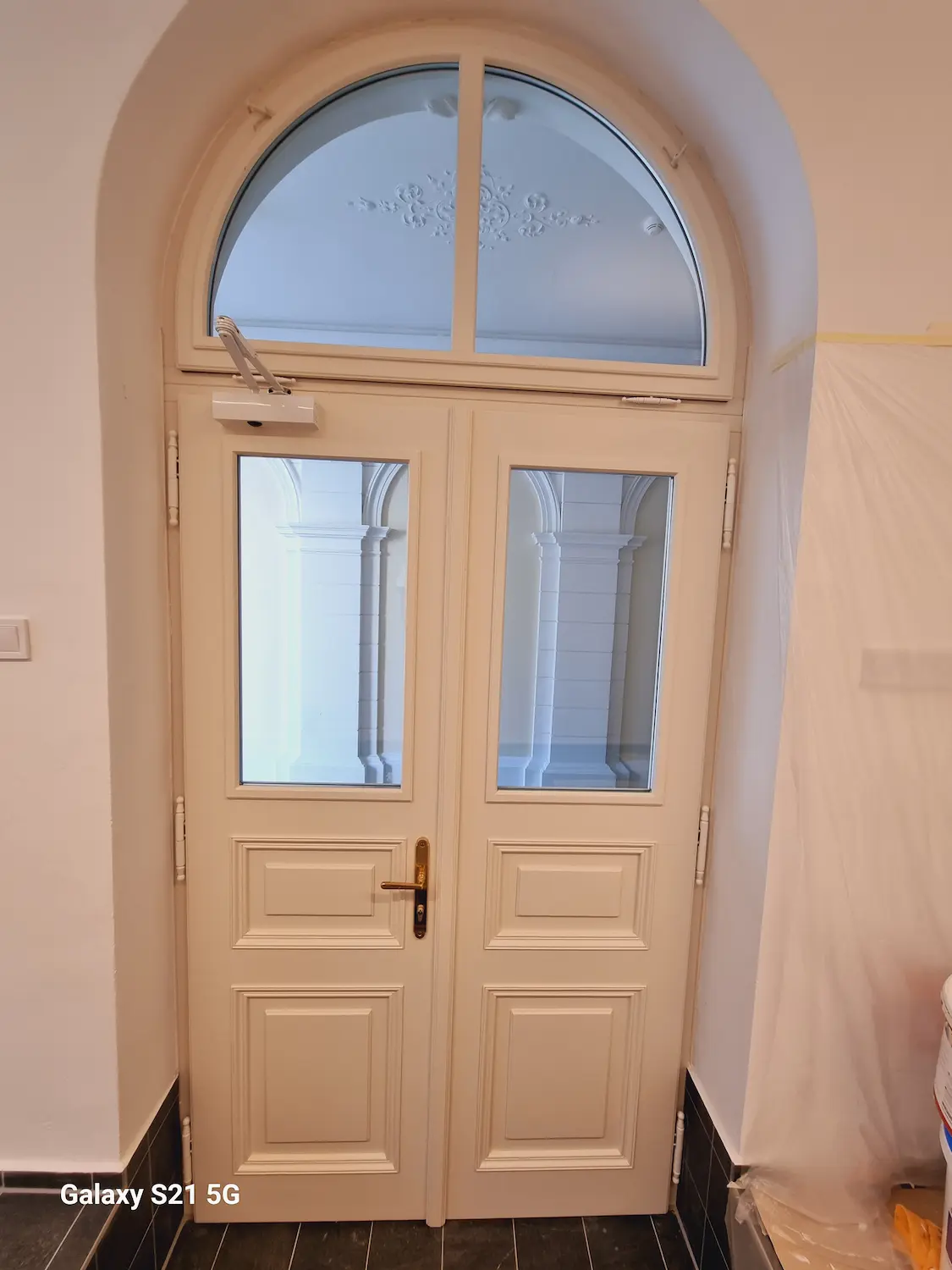 Záber na vchodové dvere zvnútra, ktoré prepúšťajú denné svetlo cez mliečne sklo.