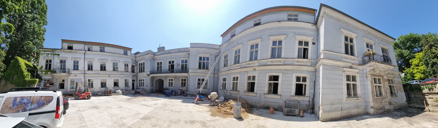 Budova v tvare polkruhu s pristaveným rebríkom, dokumentujúca postup opravy fasády.