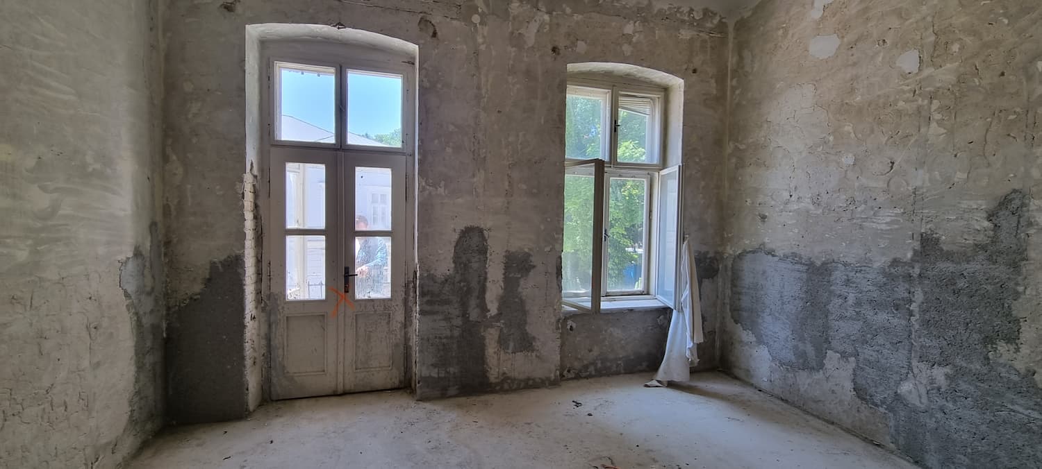 Miestnosť v procese hrubej stavby s neopracovanými stenami a osadenými bielymi kastlovými oknami.