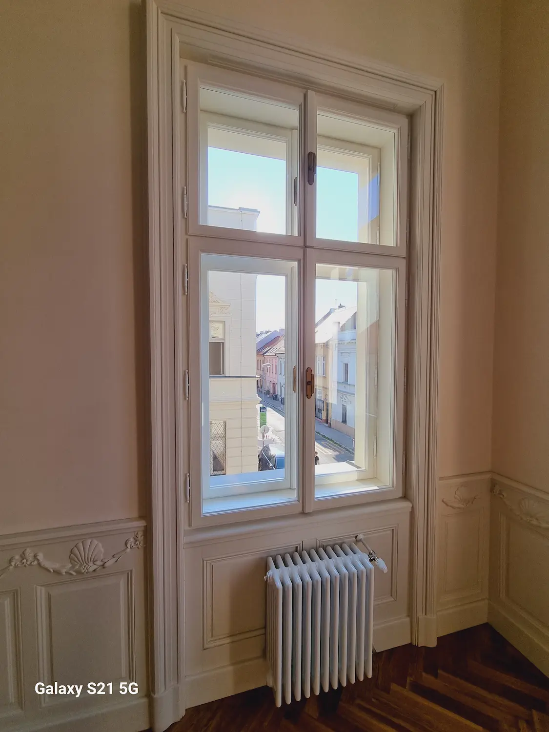 Pohľad na kastlové okno zvnútra, pod ktorým je umiestnený klasický liatinový radiátor v zrekonštruovanej miestnosti.