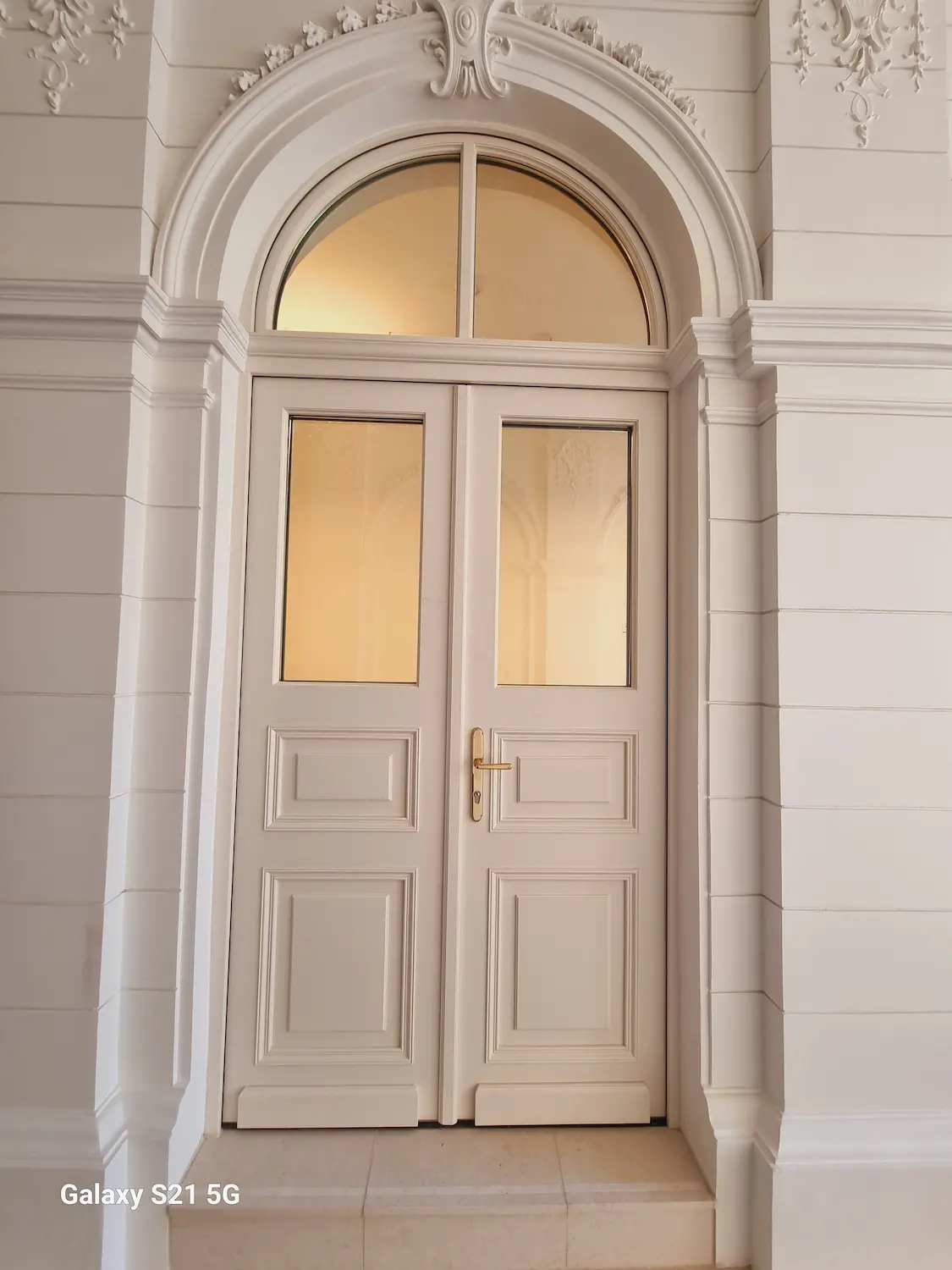 Detailné biele dvojkrídlové interiérové dvere s polkruhovým nadsvetlíkom a kazetovými výplňami.