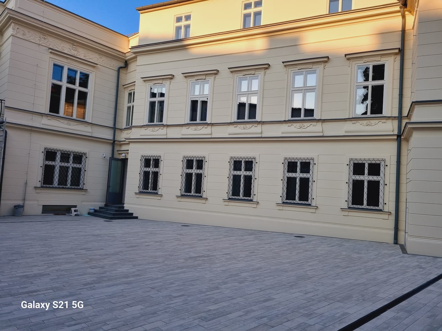 Detail dláždeného nádvoria a fasády s pravidelným členením kastlových okien v historickom štýle.