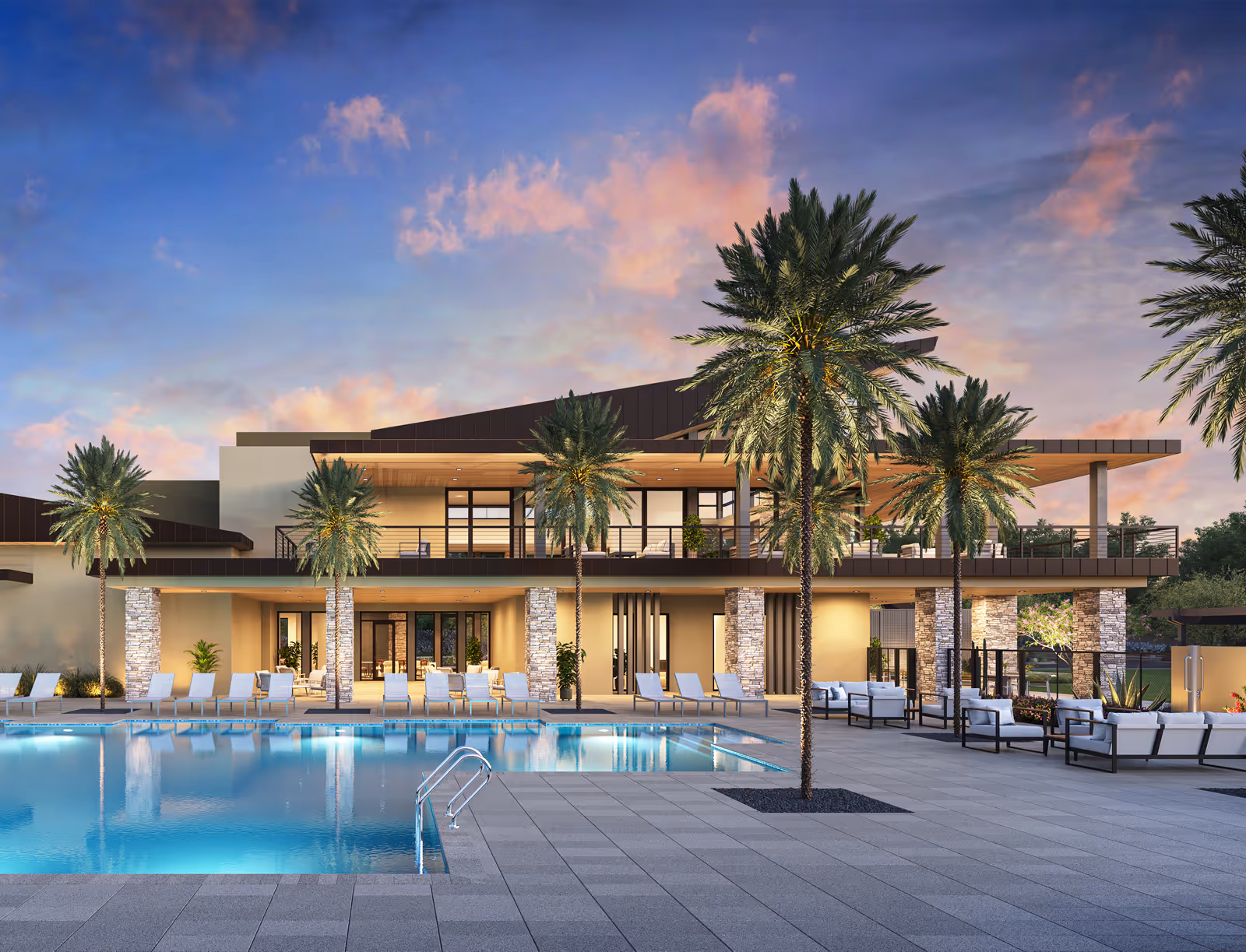 Modern clubhouse with ground floor and upper balcony overlooking a swimming pool, surrounded by palm trees and outdoor lounge chairs at sunset.