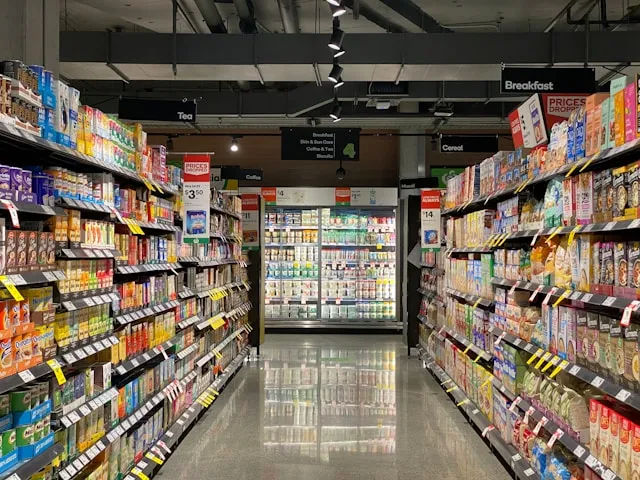 A grocery store aisle stocked with various breakfast cereals and tea products, with refrigerated items visible at the end.