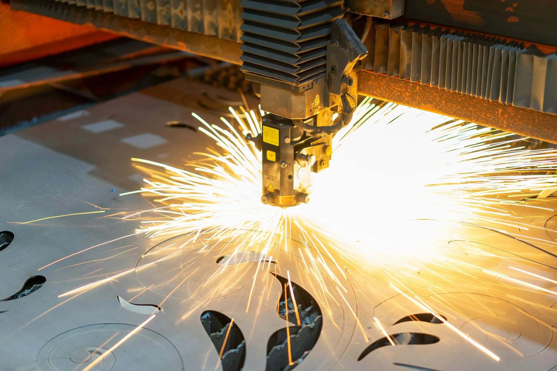 Industrial laser cutting metal sheet with bright sparks flying.