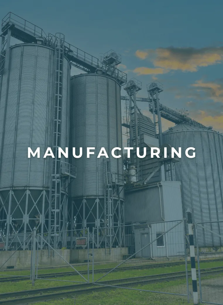 Large industrial metal silos and processing equipment at a manufacturing facility under a blue sky with clouds.