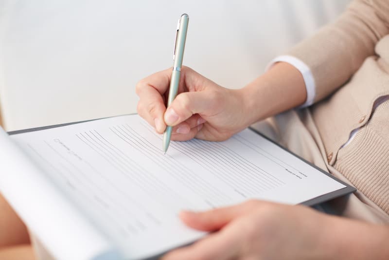 Person holding a pen and writing on a clipboard with blank lined paper.